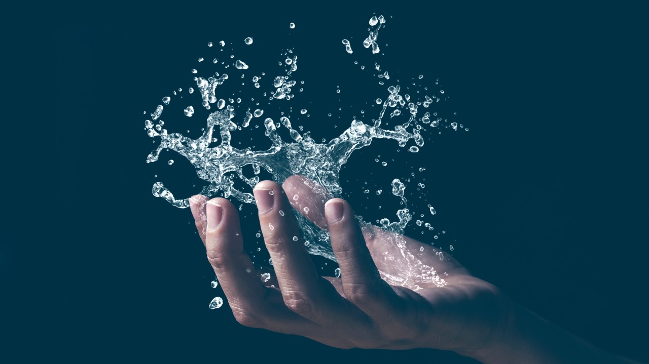 A close-up of a human hand catching or releasing splashing water droplets against a dark background.